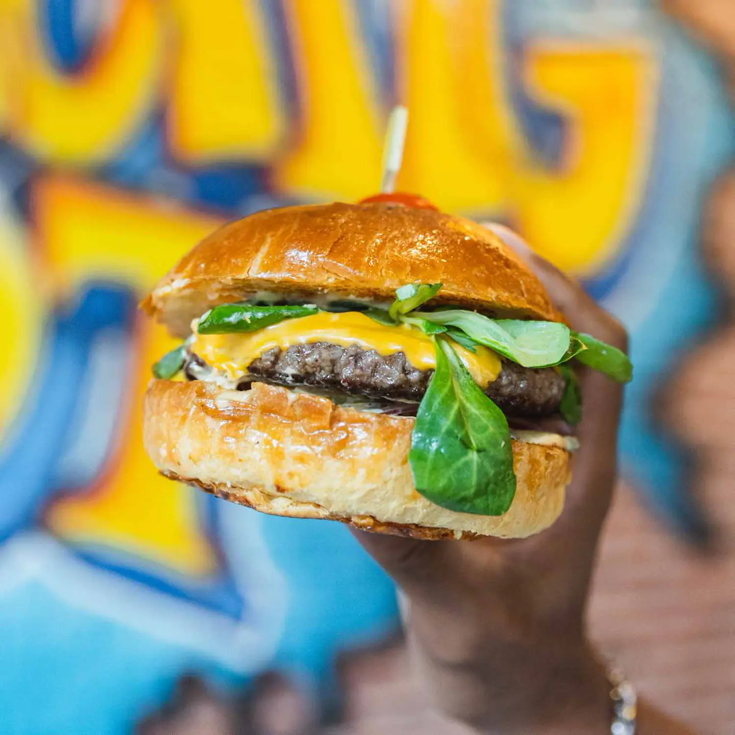 Burger maison tenu devant une fresque graffiti colorée
