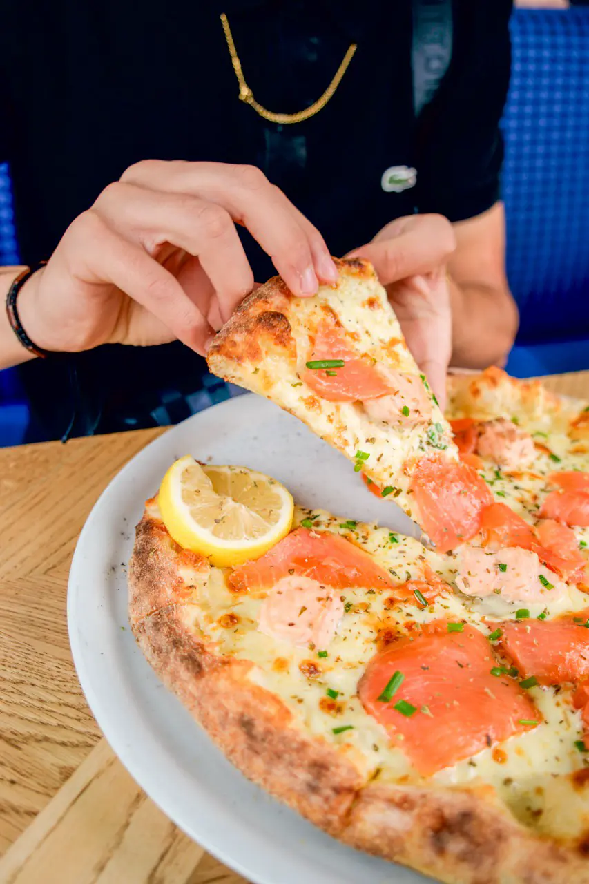Part de pizza napolitaine au saumon tenue à la main